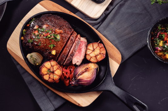 a tram wooden board with a cast iron pan filled with delicious food on top of it