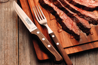 This is an image of a wooden cutting board with steak slices on the right hand side and a steak knife and fork just on the edge of the cutting board on the left
