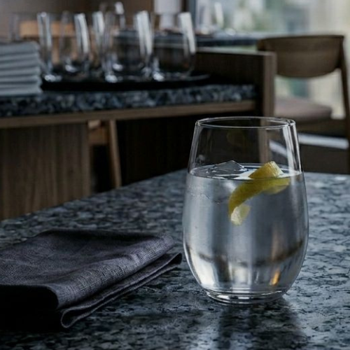 Tumbler glass filled with water and a piece of lemon zest on a table